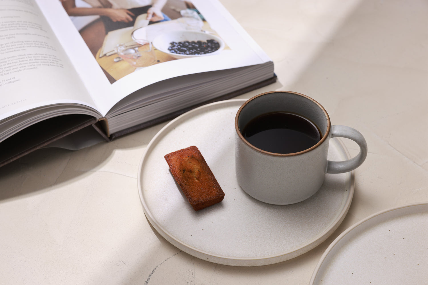 Cup of coffee on a stoneware mug with a book and dessert in the background