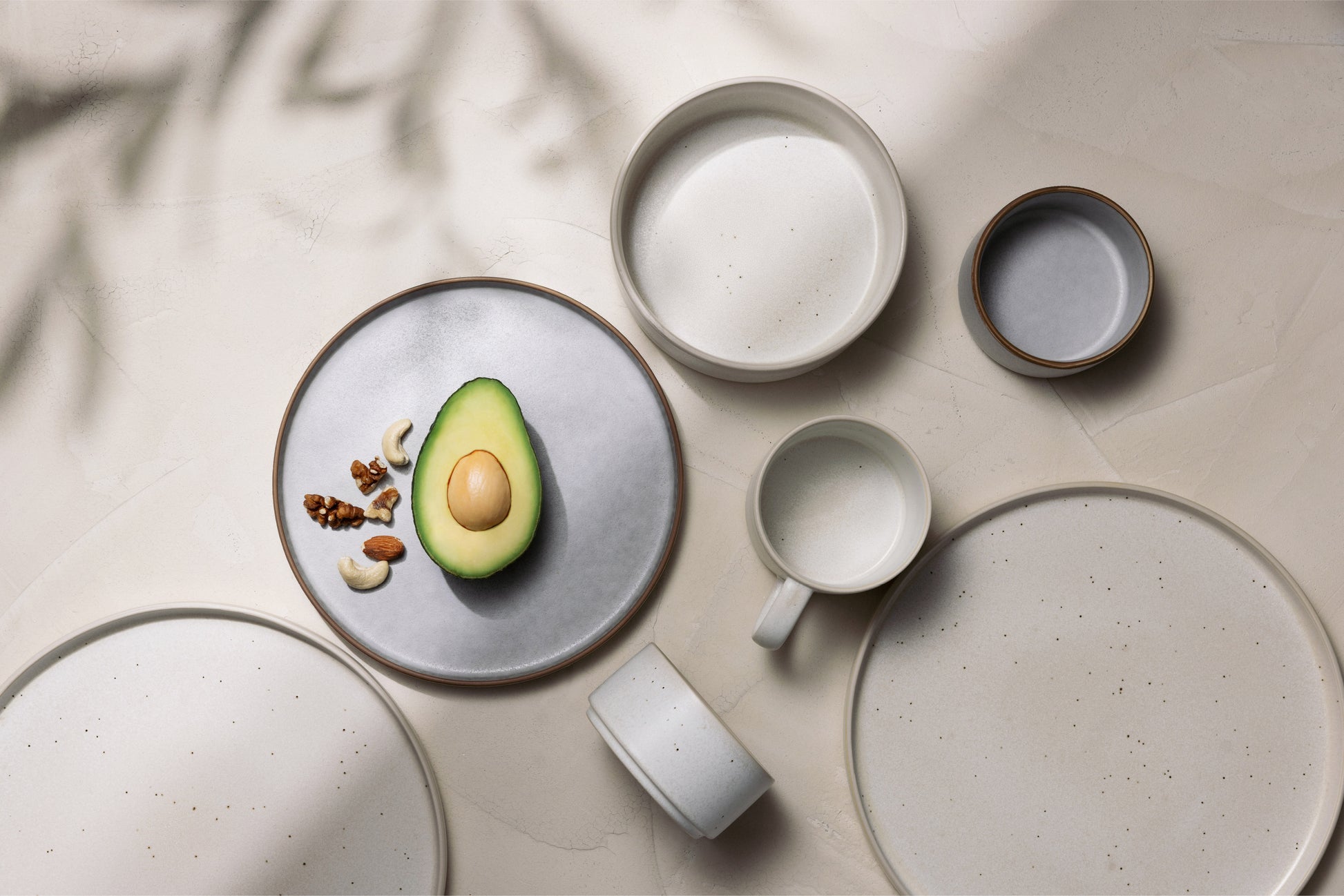 Stoneware bowls and plates with a matte finish, arranged together in neutral tones with an avocado